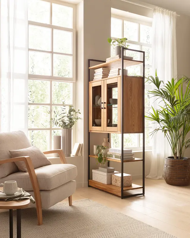 Holzvitrine neben hellem Sessel, Zimmerpflanze und großen Fenstern
